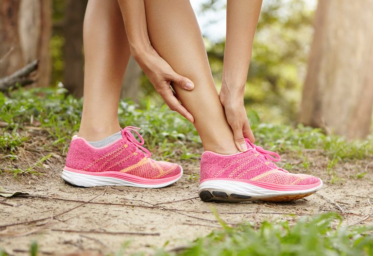 running sport injury female athlete jogger wearing pink sneakers touching her twisted or sprained ankle while jogging or running outdoors 1